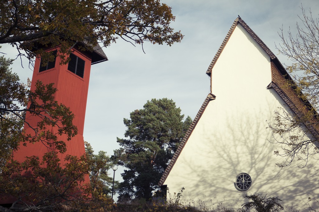 Stora Sköndals kyrkas vita gavel och röda klocktorn, omgivet av tallar.